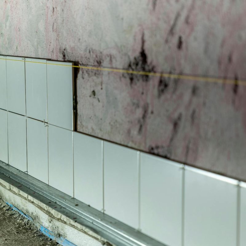 Close-up of partially tiled wall in a construction area, showcasing incomplete renovation work.