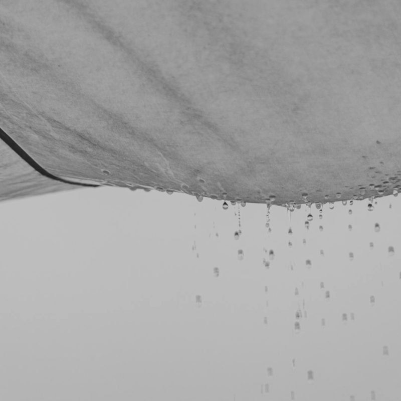 Black and white close-up of rainwater dripping off a fabric edge, creating a minimalist and abstract visual effect.